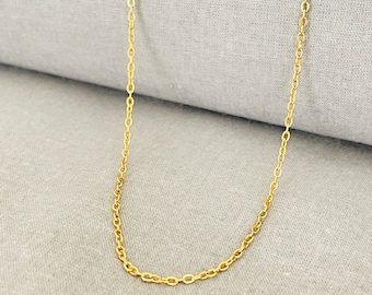 May include: A gold chain necklace on a gray fabric background.