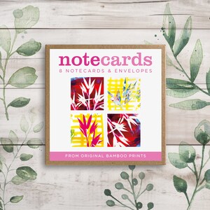 May include: A box of 8 notecards and envelopes featuring abstract floral designs in shades of red, yellow, and white. The box is brown with the text "notecards" in pink and "8 notecards & envelopes" in black. The text "FROM ORIGINAL BAMBOO PRINTS" is also printed on the box in black.