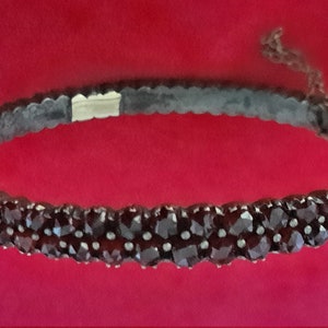 K&ouml;nnte beinhalten: Ein silbernes Armband mit einer Reihe dunkelroter Granatsteine. Das Armband besteht aus kleinen, runden Steinen, die eng aneinandergereiht sind.