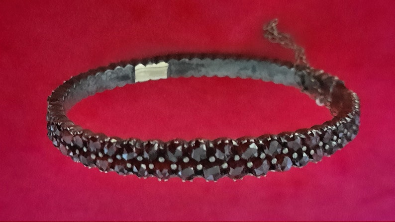 K&ouml;nnte beinhalten: Ein silbernes Armband mit einer Reihe dunkelroter Granatsteine. Das Armband besteht aus kleinen, runden Steinen, die eng aneinandergereiht sind.