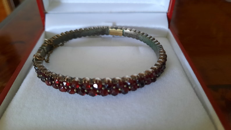 K&ouml;nnte beinhalten: Ein silbernes Armreif-Armband mit einer Reihe roter Granatsteine.