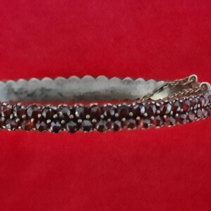 K&ouml;nnte beinhalten: Ein silbernes Armreif-Armband mit einer doppelten Reihe dunkelroter Granatsteine.