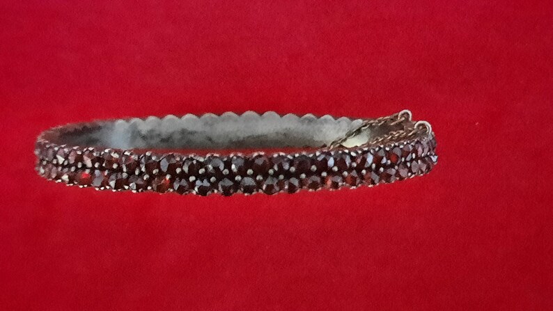 K&ouml;nnte beinhalten: Ein silbernes Armreif-Armband mit einer doppelten Reihe dunkelroter Granatsteine.