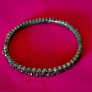 K&ouml;nnte beinhalten: Ein silbernes Armreif-Armband mit einer Reihe dunkelroter Edelsteine.