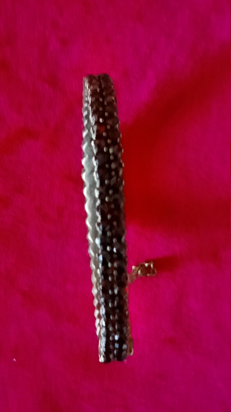 K&ouml;nnte beinhalten: Ein silbernes Armband mit einer Reihe kleiner, dunkler Steine. Das Armband liegt auf einem rosa Hintergrund.
