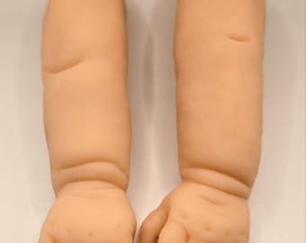 Può includere: Due braccia di bambola realistiche, color carne, con mani. Le braccia sono leggermente piegate ai gomiti e le mani sono aperte, con dita e nocche dettagliate. Le braccia sono realizzate in un materiale morbido.