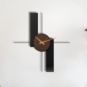 Pode incluir: Um relógio de parede moderno com um mostrador redondo de madeira castanha e ponteiros dourados. O relógio está inserido num design geométrico preto. O texto "BLACK. WALDECOR" está no canto superior direito. O relógio está montado numa parede branca.