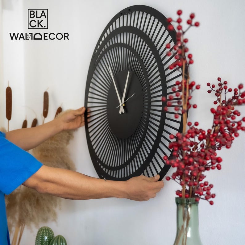 Side view of installing a large modern black metal wall clock on a white wall, showing lightweight design and easy mounting.