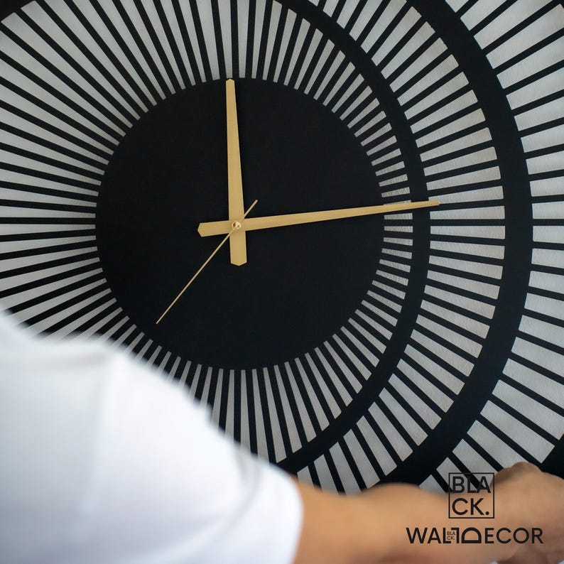 Close-up of modern black metal wall clock with gold hands and matte electrostatic finish, triple circle detailing.