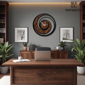 May include: A wooden desk with a laptop, a mug, and a notebook. A large, circular wall clock with a spiral design hangs on the gray wall. Two framed pictures of trees are on the wall. The clock has the text "BLACK. WALLDECOR".