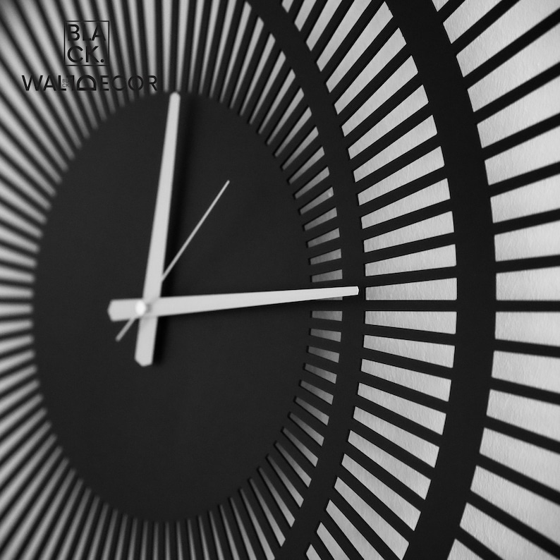 Close-up side view of black metal wall clock with silver hands, showing geometric triple circle pattern and texture.