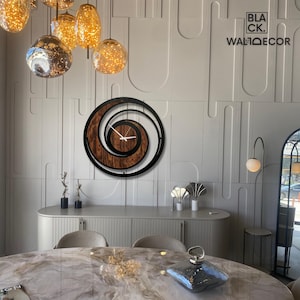 May include: A modern wall clock with a spiral design. The clock features a black frame, a wooden center, and white clock hands. The clock is mounted on a light gray wall. The text "BLACK. WALLDECOR" is visible in the upper right corner.