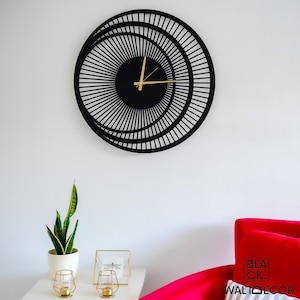 Modern black metal wall clock on white wall with red chair and console, elegant decor for entryway or living room.