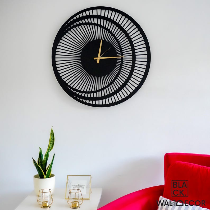 Modern black metal wall clock on white wall with red chair and console, elegant decor for entryway or living room.