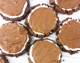 May include: A close-up of several chocolate cookies with a white frosting center. The cookies are arranged on a white surface.