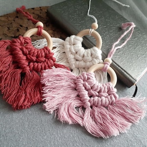 Peut inclure: Trois tentures murales en macramé avec des anneaux en bois. Les tentures sont rouge, blanche et rose avec des franges.