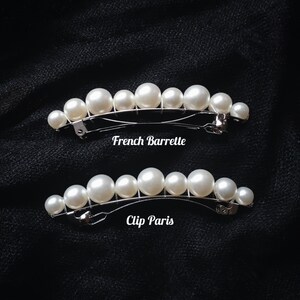 K&ouml;nnte beinhalten: Zwei silberne Haarklammern mit einer Reihe wei&szlig;er Kunstperlen. Die obere Klammer ist mit "French Barrette" und die untere mit "Clip Paris" beschriftet.