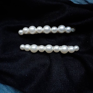 White textured pearls laced onto a silver french barrette (not pictured here), with transparent string. They are laying on top of black and blue fabric.