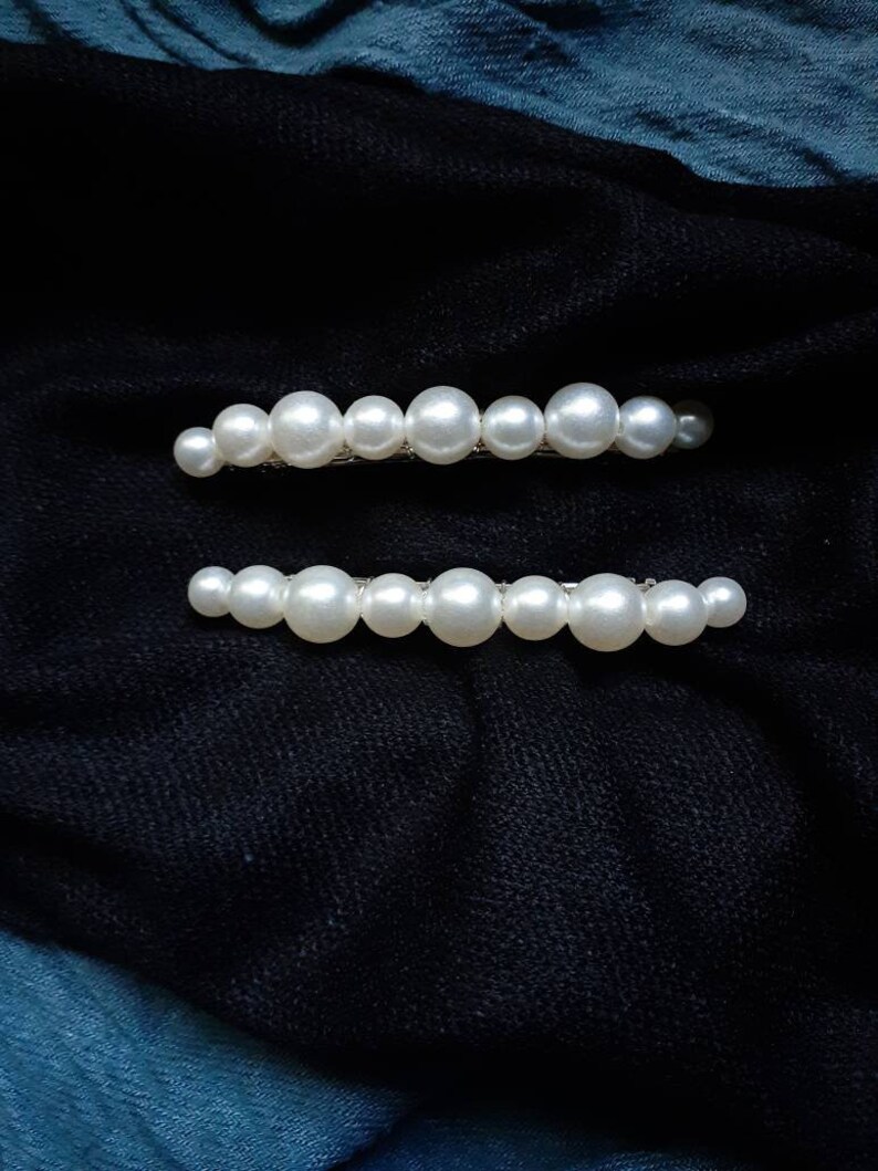 White textured pearls laced onto a silver french barrette (not pictured here), with transparent string. They are laying on top of black and blue fabric.