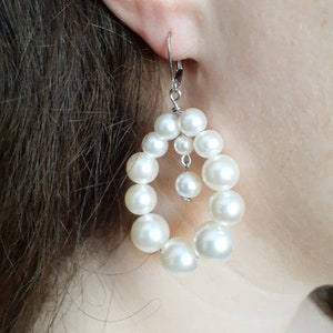 Peut inclure: Une paire de boucles d'oreilles en perles blanches en forme de larme. Les boucles d'oreilles sont composées d'une chaîne de perles avec une perle plus petite qui pend en bas.