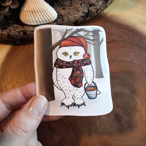 Harfang des neiges transportant du sirop d'érable dans un seau marchant à travers la forêt. Animal de l'Arctique canadien. Autocollant symbolique.  Laminé résistant à l'eau
