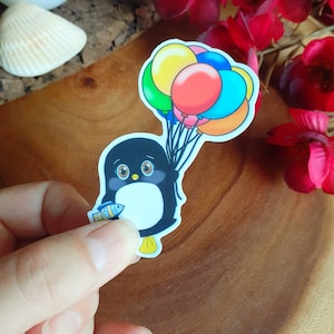 Petit pingouin avec poisson accroché à des ballons ; Autocollant en vinyle. Ballons colorés. Noeud papillon noir et blanc. Art d'oiseau adorable.