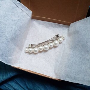 First Variation Option. One pearl barrette in petite cardboard box with white tissue paper. Black and blue fabric in background.