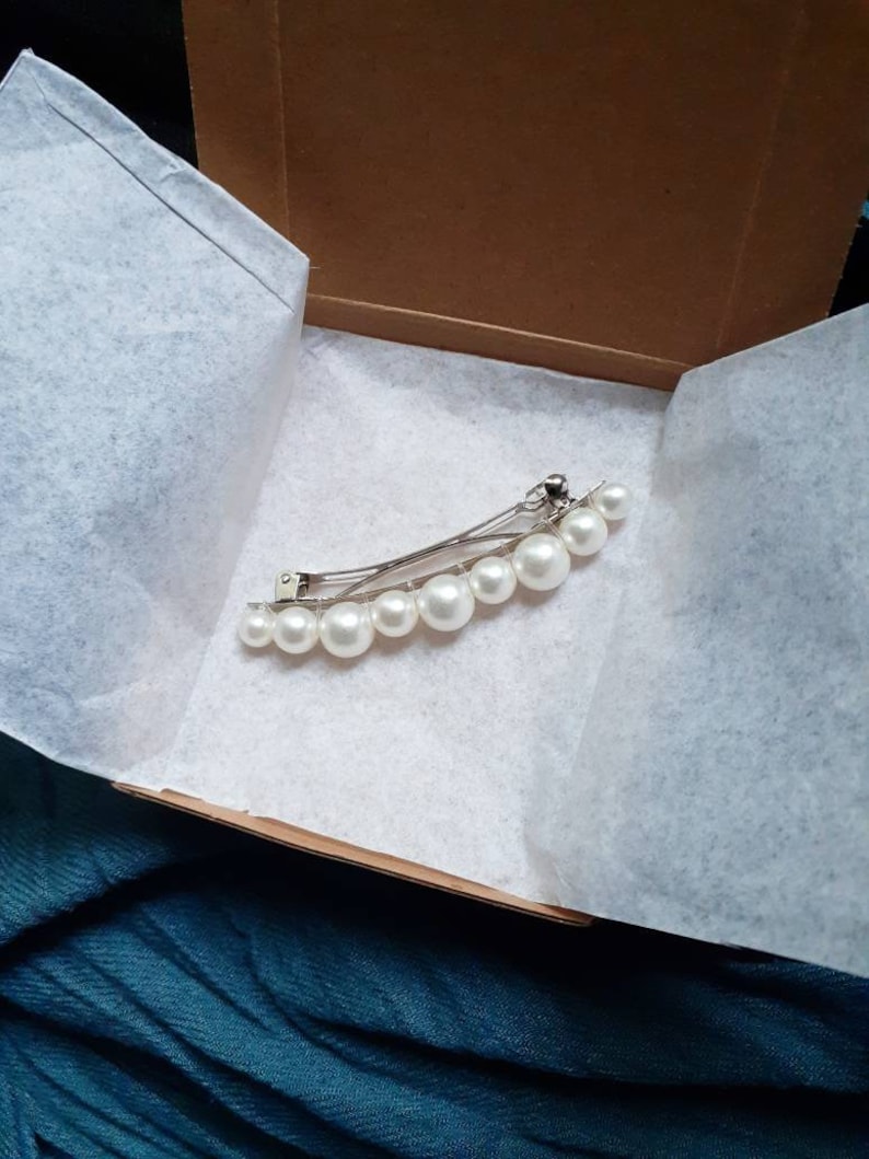 First Variation Option. One pearl barrette in petite cardboard box with white tissue paper. Black and blue fabric in background.