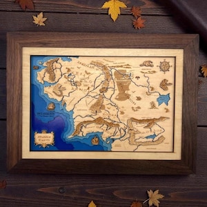 May include: Wooden framed map of Middle Earth, featuring a detailed laser-cut design. The map shows the topography with varying depths of blue for the sea and brown for the land. The frame is a dark brown color.