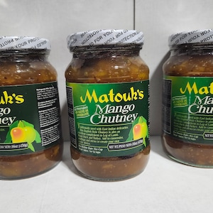 May include: Three glass jars of Matouk's Mango Chutney, each with a green label featuring yellow text and a mango illustration. The jars have white screw-on lids with a tamper-evident seal. Each jar contains 16 ounces of golden-brown chutney.