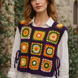 Puede incluir: Un chaleco de crochet morado con patrones cuadrados coloridos. Los cuadrados presentan diseños naranjas, amarillos, verdes y blancos. El chaleco tiene lazos laterales y se usa sobre una camisa blanca abotonada y unos vaqueros azules. El estilo general es bohemio.