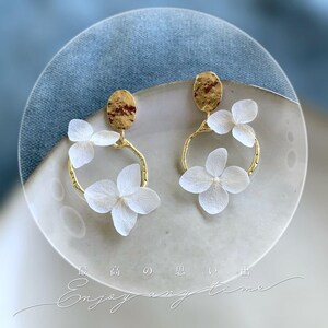 May include: Gold hoop earrings with delicate white pressed flowers. The earrings feature a hammered gold disc at the top.