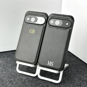 May include: Two black leather phone cases with a silver kickstand. The cases have the initials "GB" and "MS" embossed on them.
