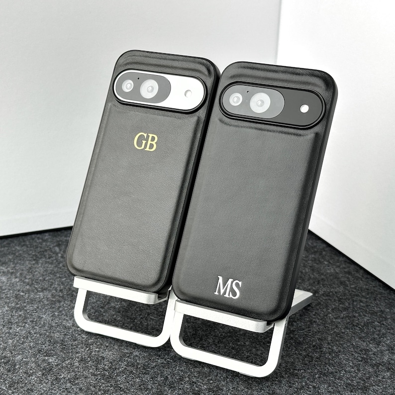 May include: Two black leather phone cases with a silver kickstand. The cases have the initials "GB" and "MS" embossed on them.