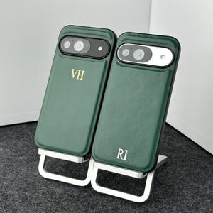 May include: Two green leather phone cases with black camera cutouts and gold lettering. The case on the left says "VH" and the case on the right says "RI".