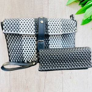 May include: A set of two woven bags, one larger than the other. The larger bag is black and white with a black leather strap and buckle. The smaller bag is black and has a woven texture. Both bags have a woven design.