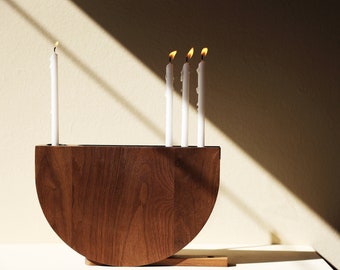 May include: A wooden candle holder with a half-circle shape, holding five white candles, four of which are lit.