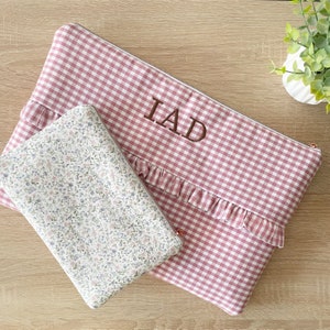 Peut inclure: Deux pochettes zippées en tissu vichy rose et blanc. La plus grande pochette a un bord festonné et le texte "IAD" brodé dessus. La plus petite pochette a un imprimé floral.