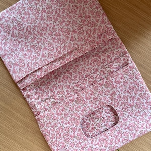 May include: A rectangular fabric case featuring a pink and white floral pattern. The case has multiple interior pockets and a rectangular cutout opening. A small rectangular label with the text MAR DESIGN is attached to the bottom left corner.