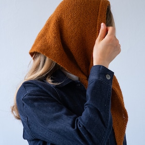 May include: A person wearing a brown hooded scarf over their head and a dark blue denim jacket.