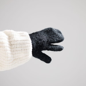Puede incluir: Una manopla de punto gris carbón oscuro con una superficie texturizada y difusa. La manopla está unida a un puño de manga de punto acanalado grueso de color crema que se extiende desde la zona de la muñeca, mostrando un contraste de colores.