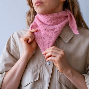 May include: A woman wearing a light brown shirt with a pink knitted scarf tied around her neck.