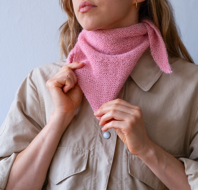May include: A woman wearing a light brown shirt with a pink knitted scarf tied around her neck.
