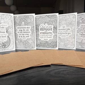 May include: A set of five white cards with black line art and inspirational quotes, paired with brown paper envelopes. The cards feature intricate designs and text from Psalms and Isaiah. The cards are suitable for coloring.