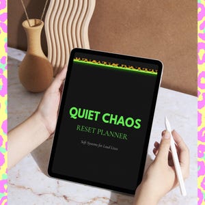 Puede incluir: Una tableta digital que muestra una pantalla negra con el texto verde brillante Quiet Chaos Reset Planner y el subtítulo Soft Systems for Loud Lives. La parte superior de la pantalla tiene un borde con estampado de leopardo y un lápiz blanco.