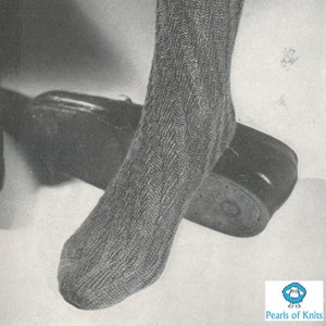 以下が含まれることがあります： ケーブル編みのパターンが付いたグレーのニットソックス2足。ソックスはモデルの脚に履いています。