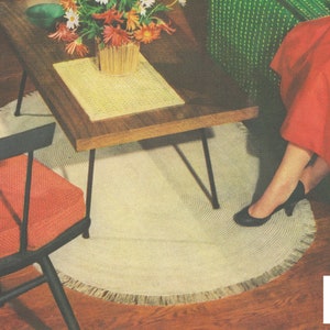 Op de afbeelding: Een wit ovaal vloerkleed met een franje rand, een zwarte houten stoel met een rood kussen, een houten salontafel met een gele placemat en een vrouw in een rode rok en zwarte schoenen die op een groene bank zit.