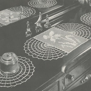 May include: Four white crocheted doilies, two round and two rectangular, are arranged on a dark wooden surface. The doilies are made with a delicate, lacy pattern. A small, round, silver-colored container sits on one of the doilies.