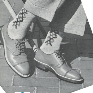 Op de afbeelding: Een paar bruine leren schoenen met witte veters en een witte zool. De schoenen worden gedragen met sokken die een geometrisch patroon in zwart, wit en grijs hebben.