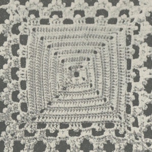 May include: A close-up of a crocheted square with a detailed, intricate pattern. The square is made of white yarn and has a delicate, lacy appearance.